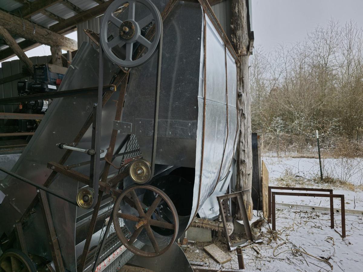 A belt-driven grain-cleaning machine with pulleys and cogs at the edge of a snowy field.